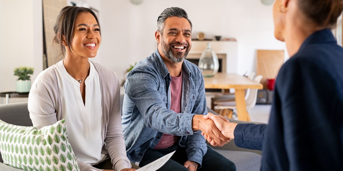 Happy couple sitting on a couch shaking hands with an insurance broker.
