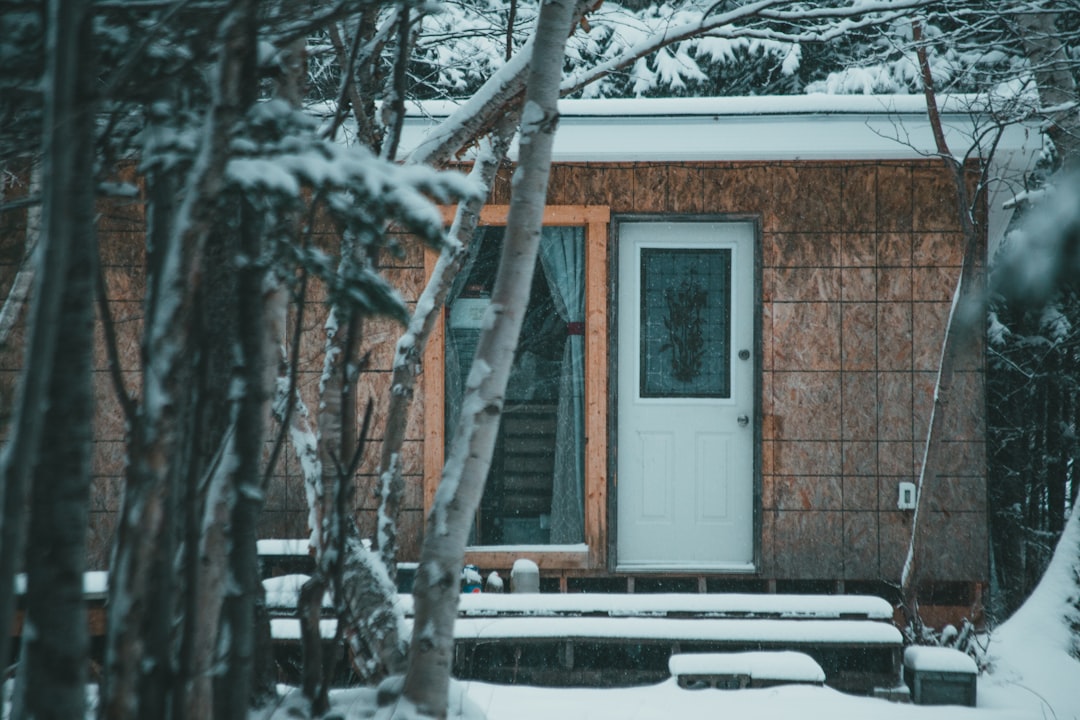 A stylishly dressed guest smiling as she uses her smartphone for keyless entry at the front door of a luxurious modern cabin in a snowy Aspen setting.