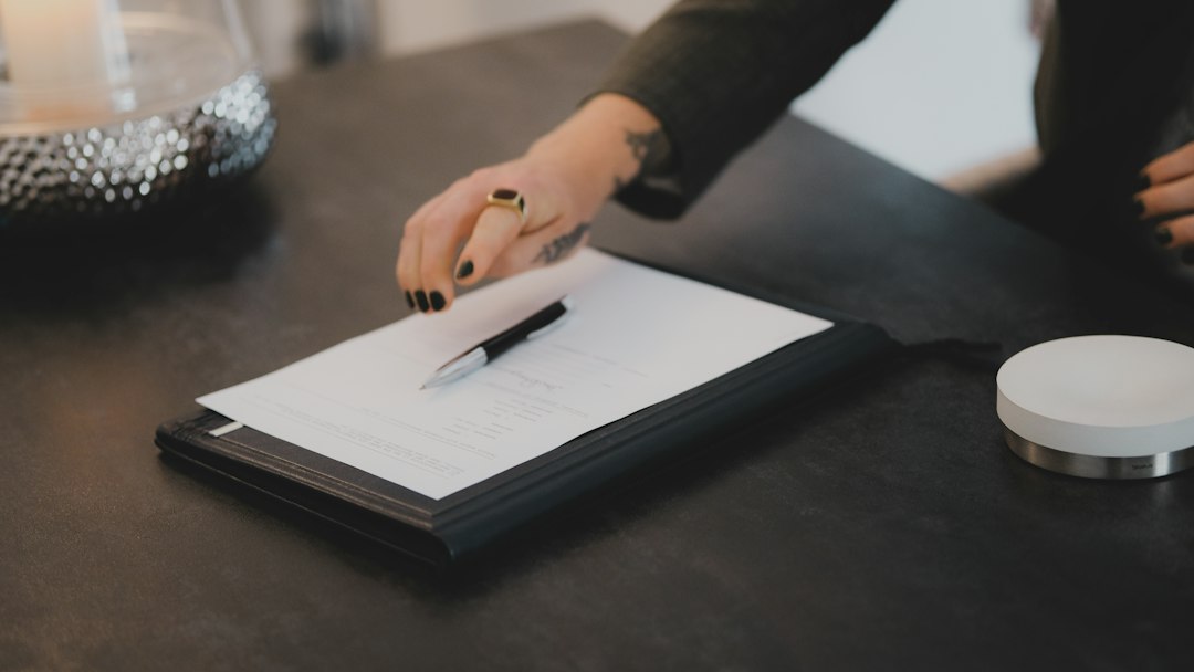 A close-up, professional shot of a person's hand signing a real estate contract with an elegant pen on a clean, modern desk.