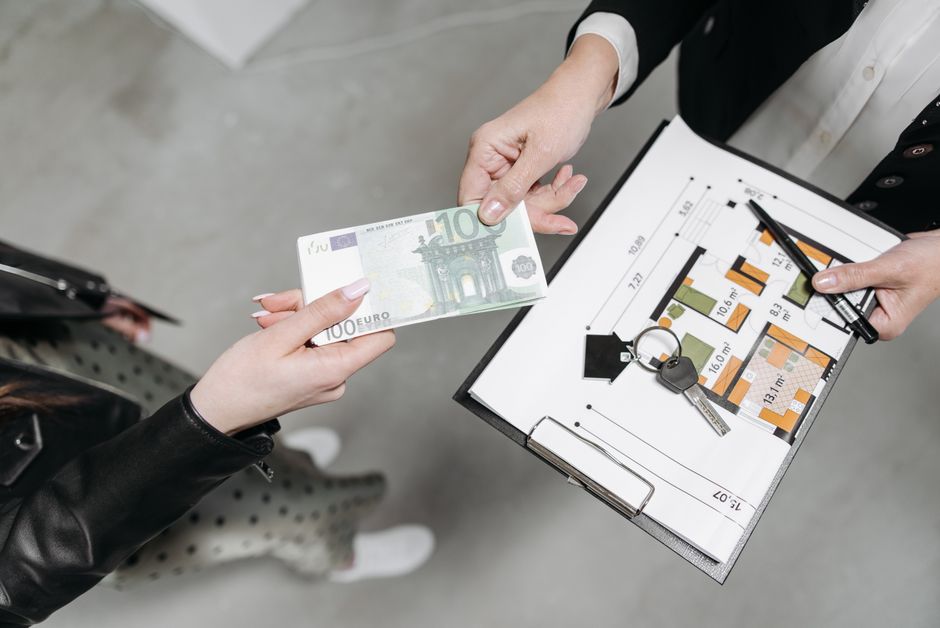 A professional real estate agent handing over a set of modern keys to a new homeowner in front of an elegant, high-end house.