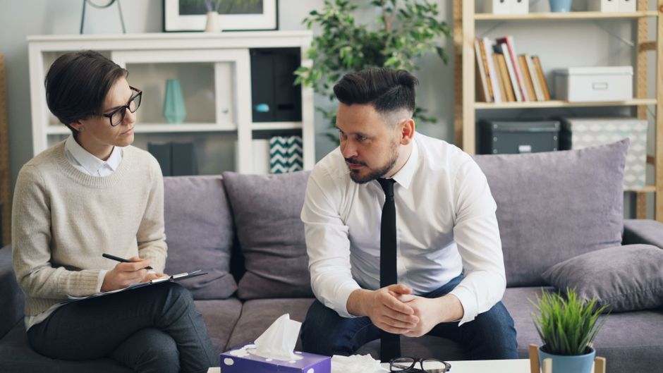 A real estate professional and a client having a serious, consultative conversation in the bright, sophisticated living room of a luxury Aspen property.